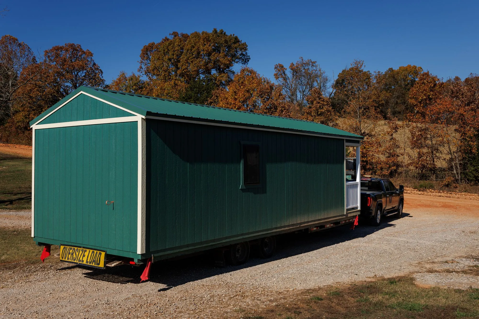 A long green building on its delivery trailer, leaving the lot for a customer