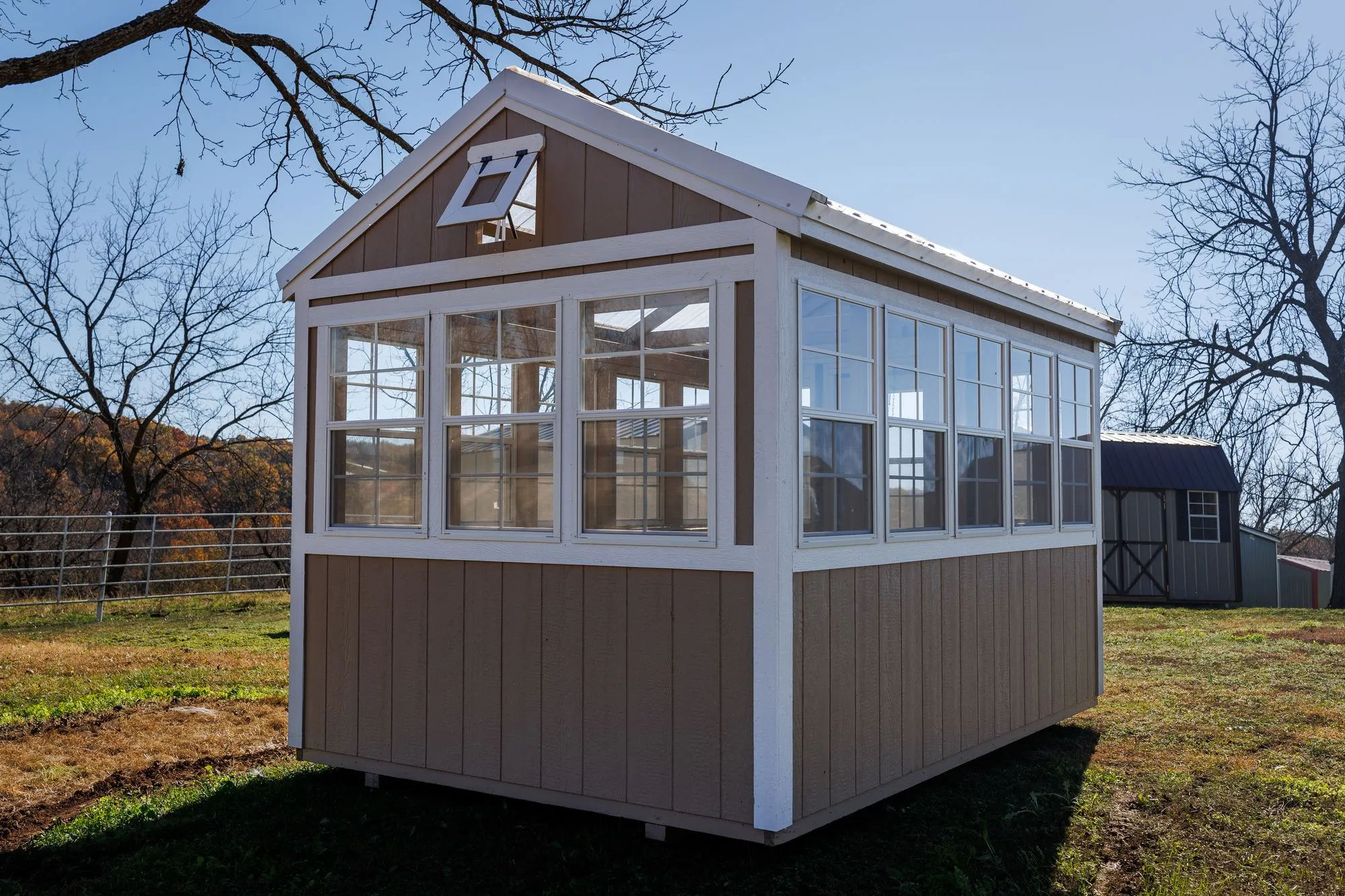 Greenhouse with tan siding with white trim and windows down both sides