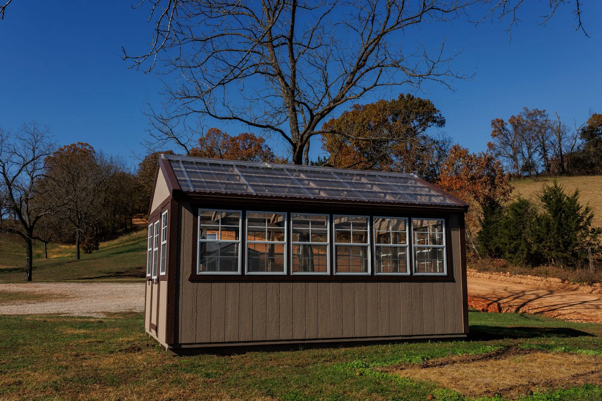 Greenhouse with tan siding with brown trim and a clear corrugated roof