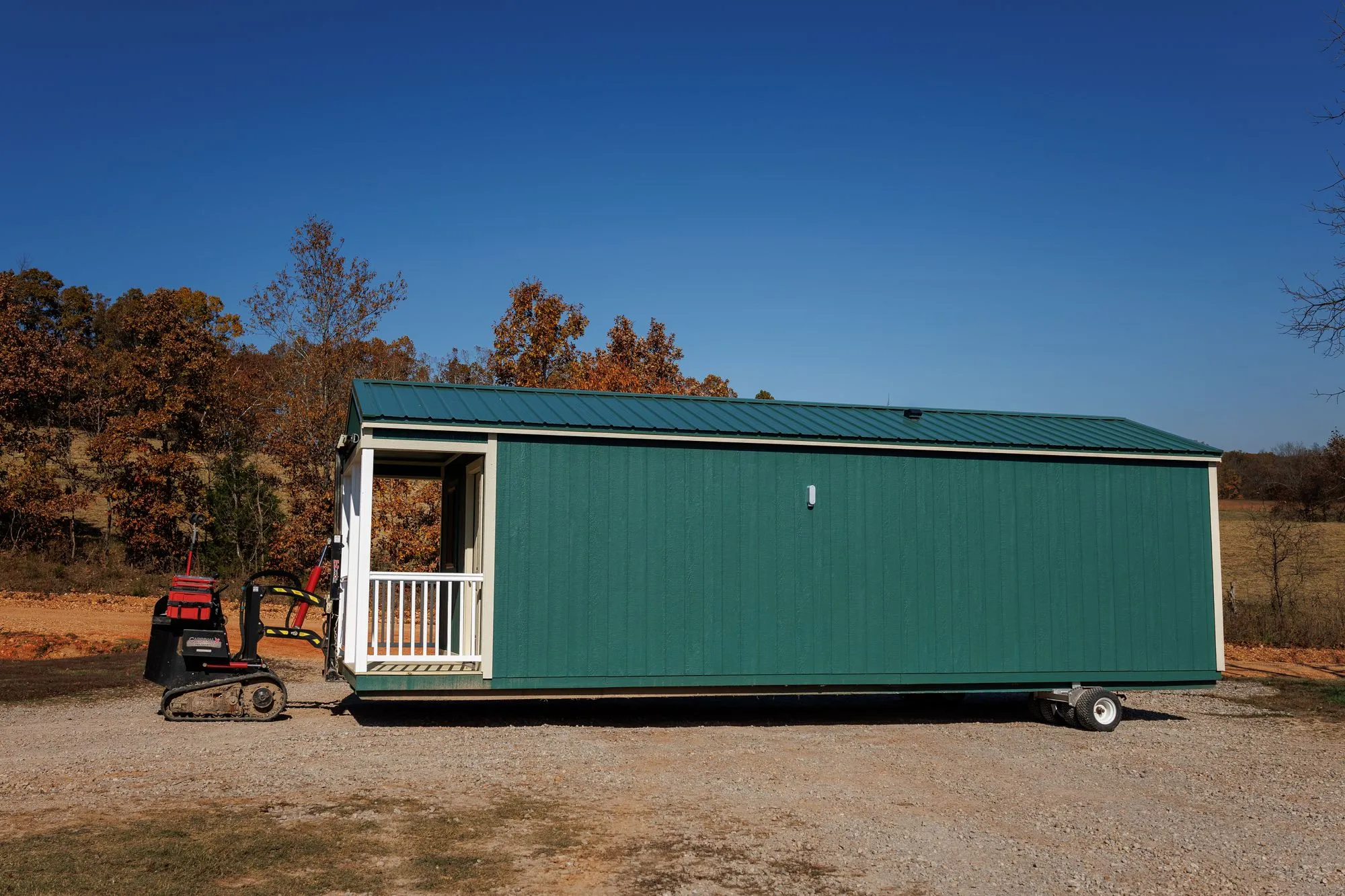 A building mover positioning a long green cabin on a gravel pad