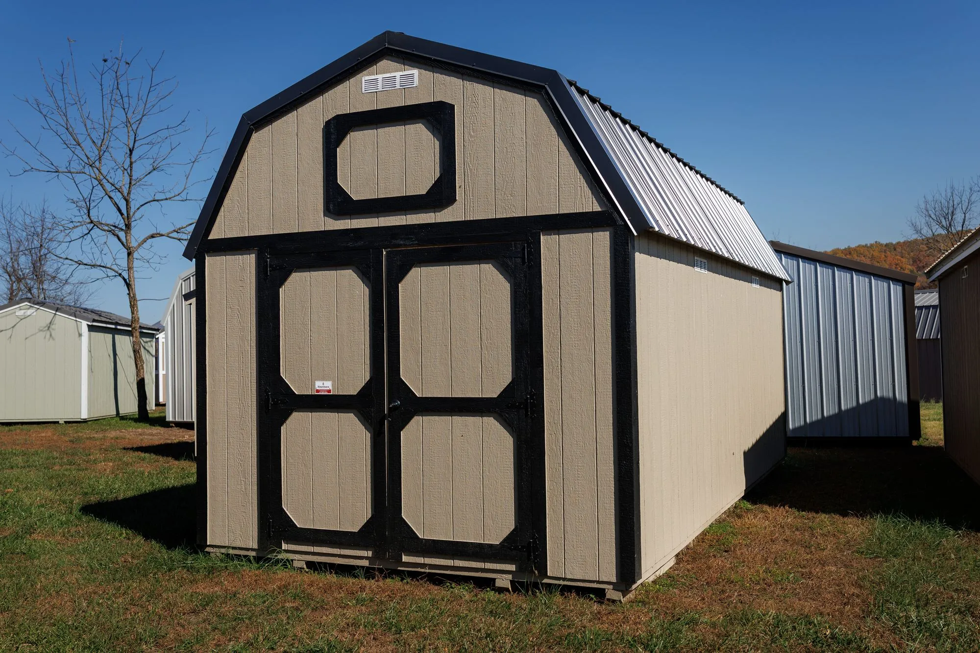 Lofted Barn with tan siding with black trim and roof, octagon-panel doors
