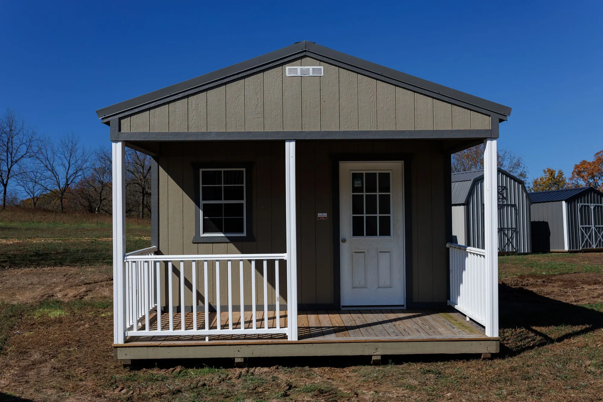 Cabin with olive-taupe siding, charcoal trim and roof, front porch with white railings