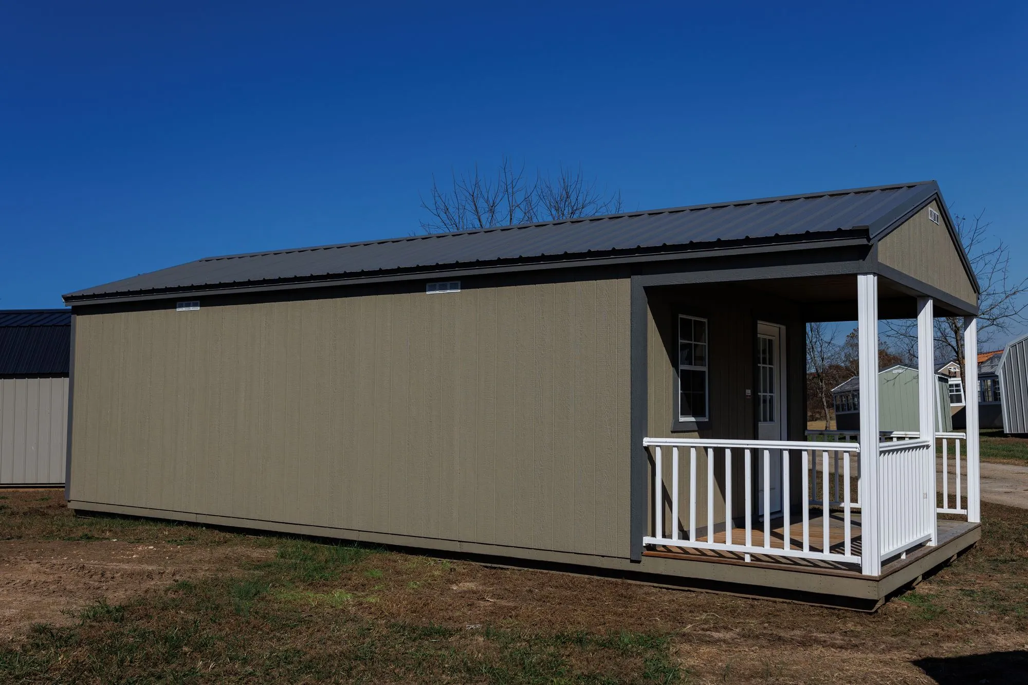 Cabin with olive-taupe siding, charcoal trim and roof, front porch with white railings