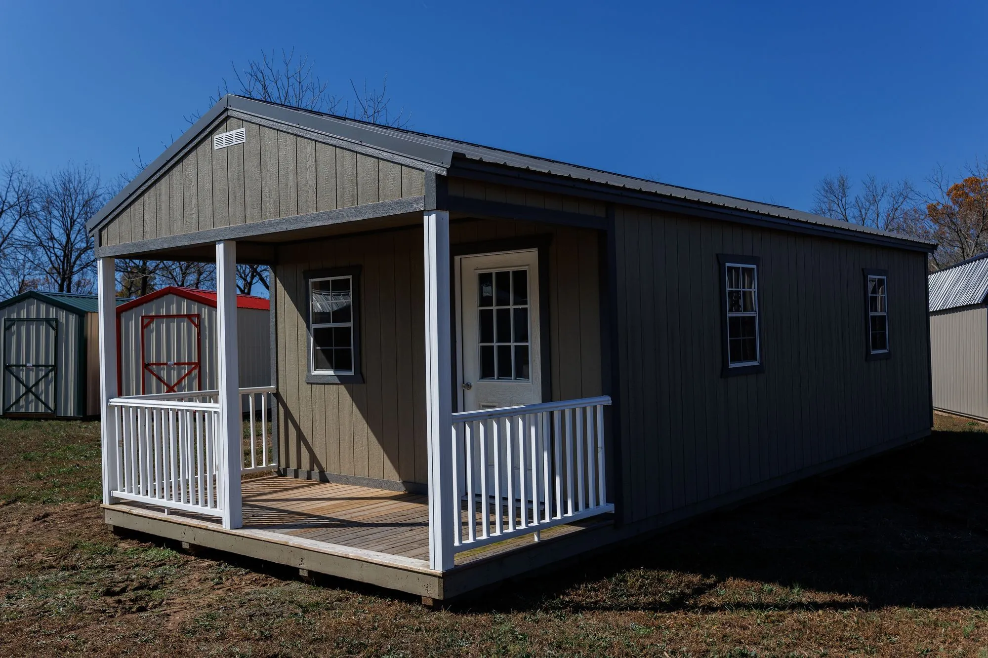 Cabin with olive-taupe siding, charcoal trim and roof, front porch with white railings