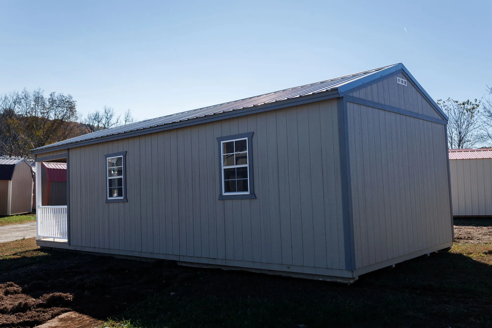 Cabin with olive-taupe siding, charcoal trim and roof, front porch with white railings