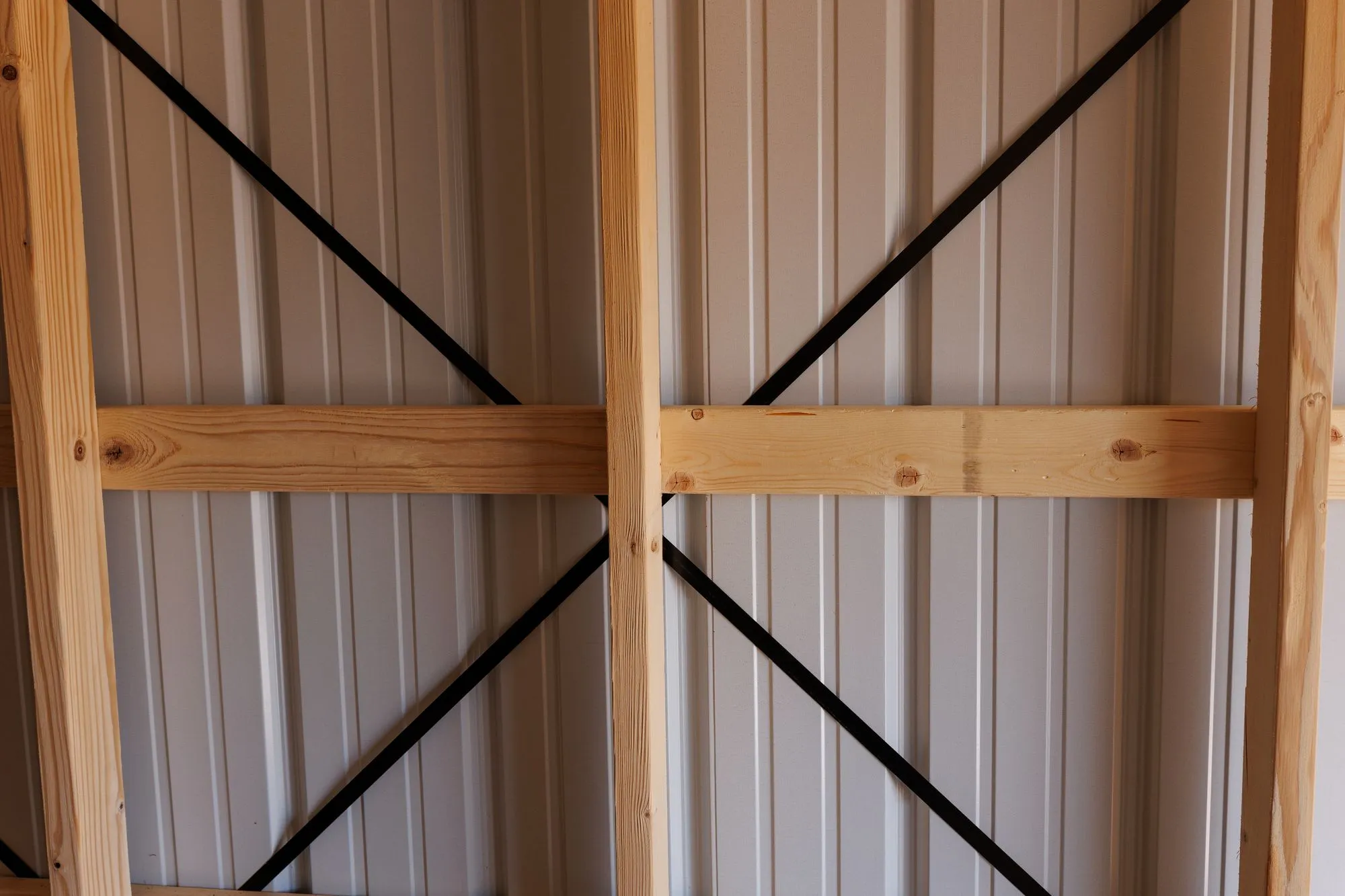 Wood wall framing with black diagonal bracing behind white metal siding inside a building