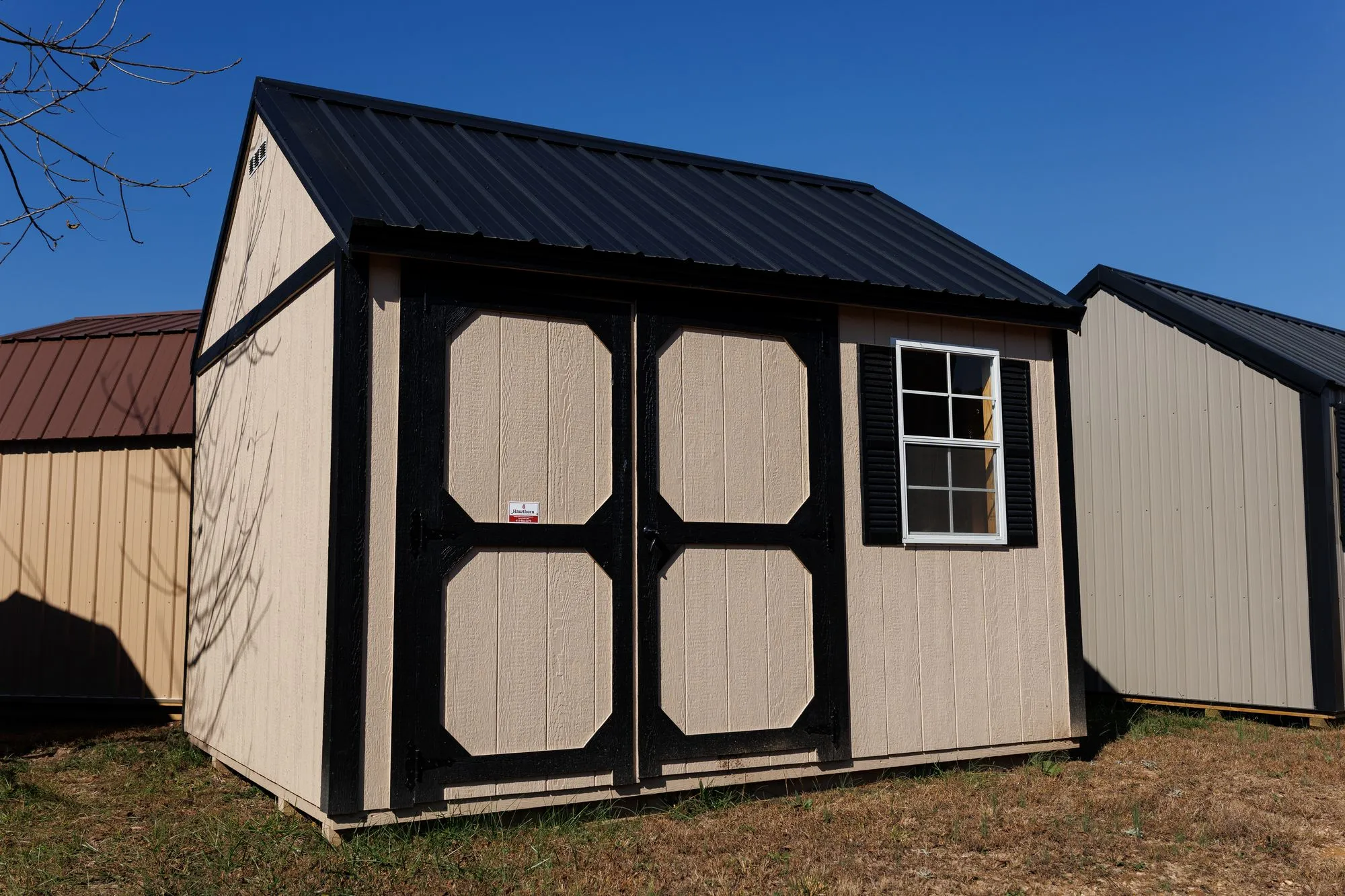 Garden Shed with tan siding, black trim and roof, black-framed octagon-panel doors