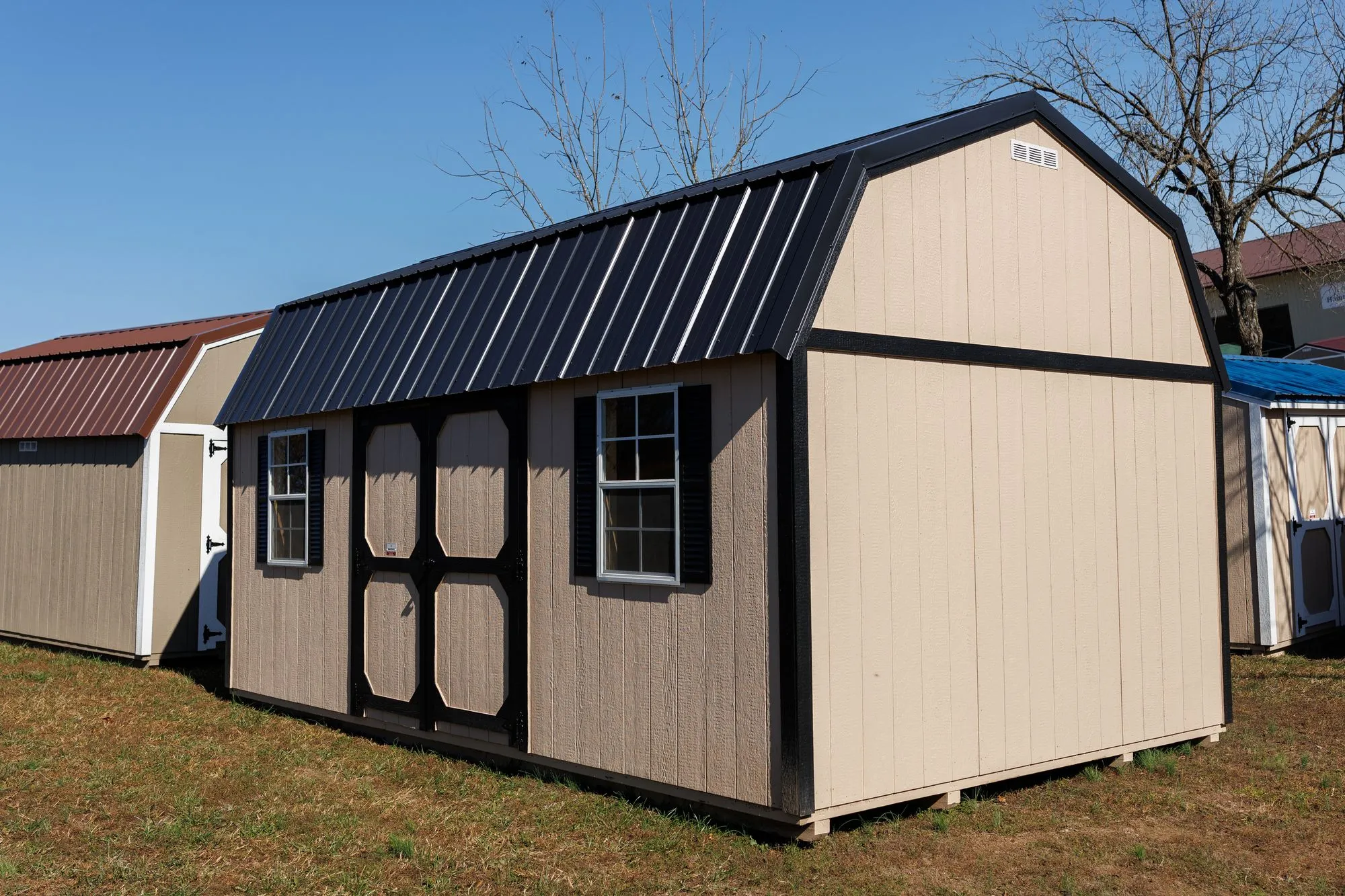 Lofted Garden Barn with tan siding, black trim and roof, octagon-panel doors