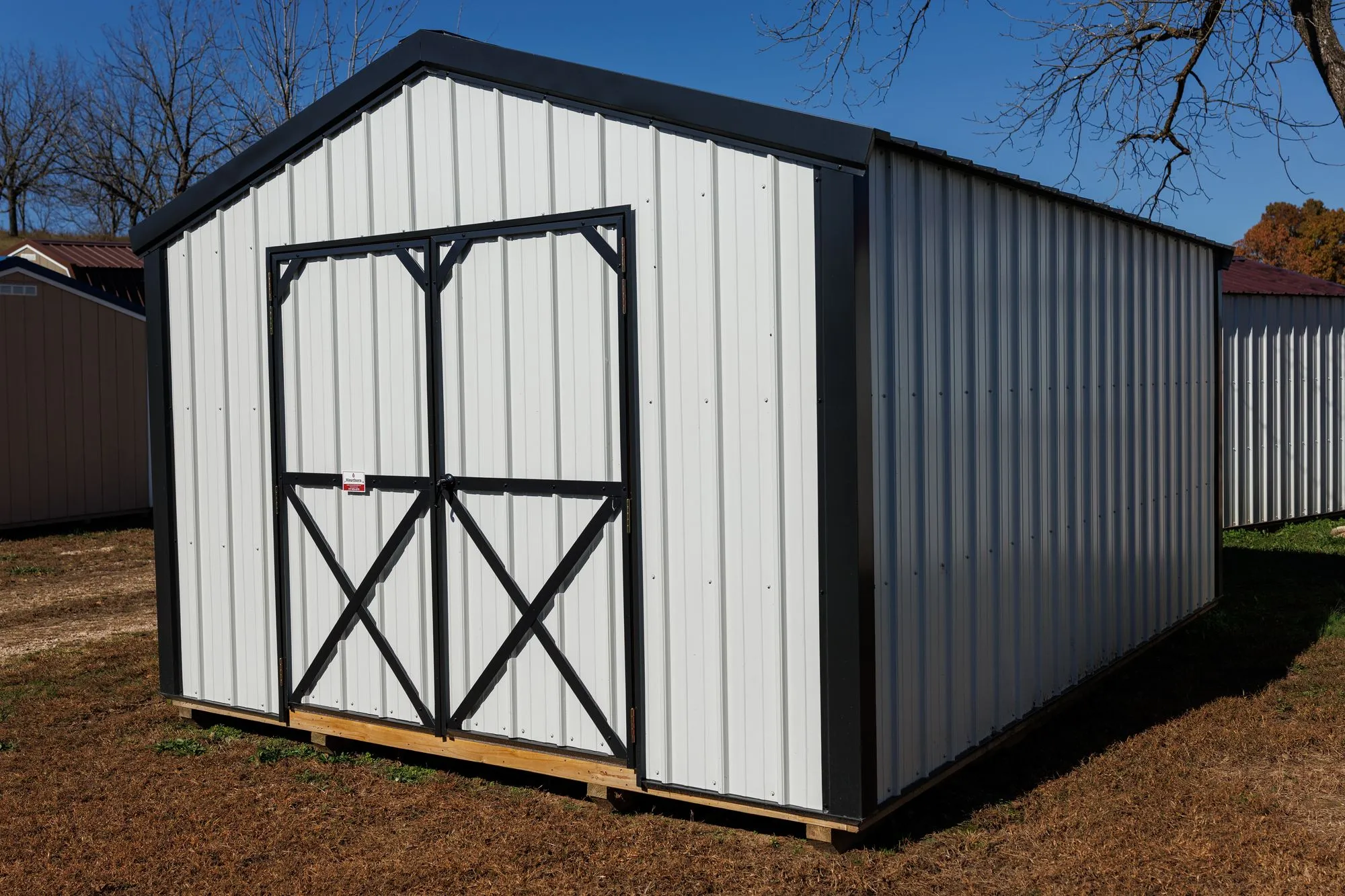 Utility Shed with white metal siding, black trim and roof, black X-braced doors