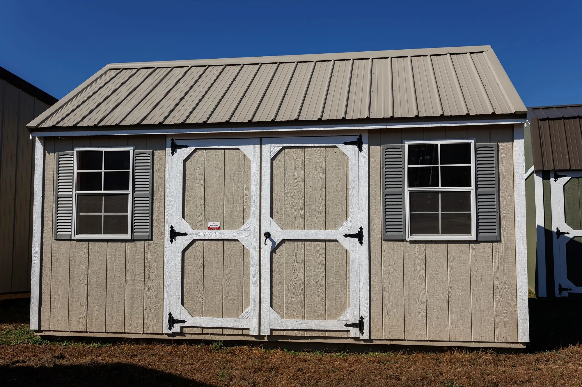 Lofted Garden Shed with tan siding, white trim, clay roof, white octagon-panel doors, two windows