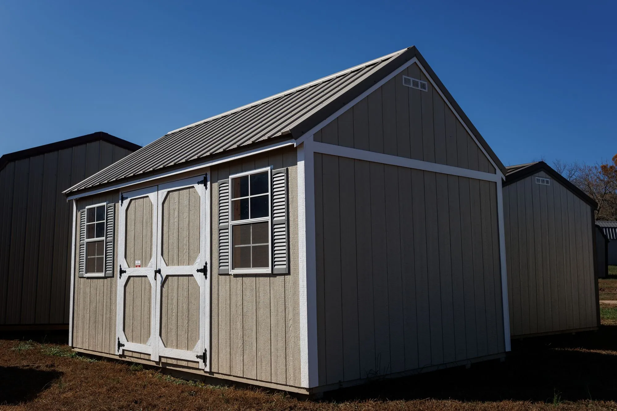 Lofted Garden Shed with tan siding, white trim, clay roof, white octagon-panel doors, two windows