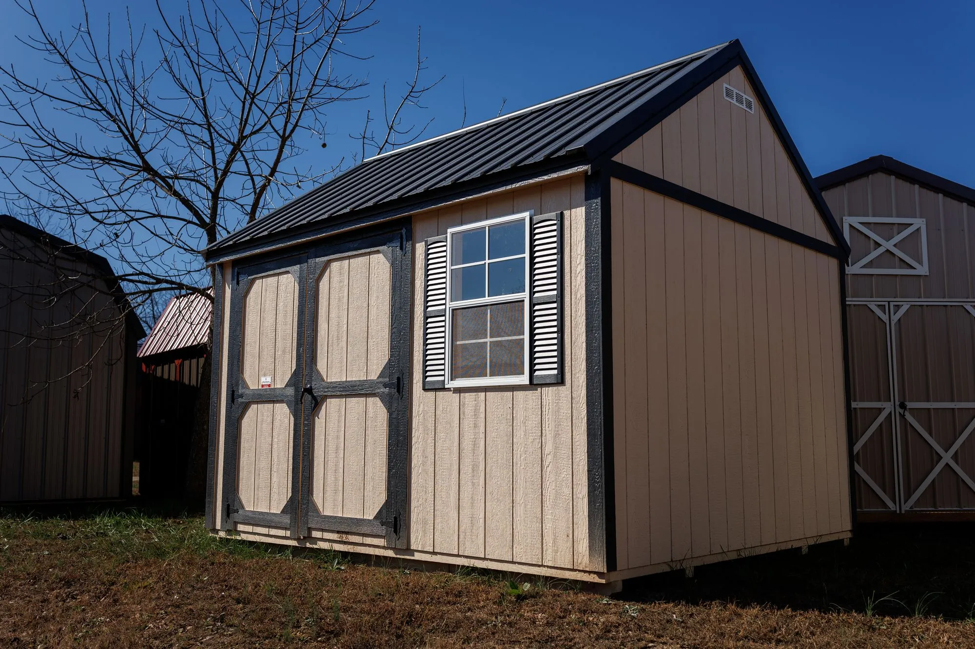 Garden Shed with tan siding, black trim and roof, black-framed octagon-panel doors