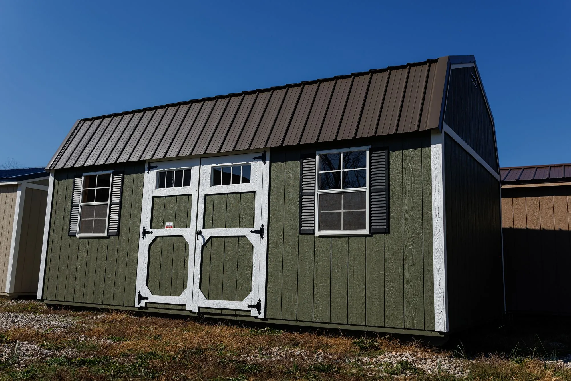 A green Lofted Garden Barn with white trim, a brown roof and white doors with transom windows