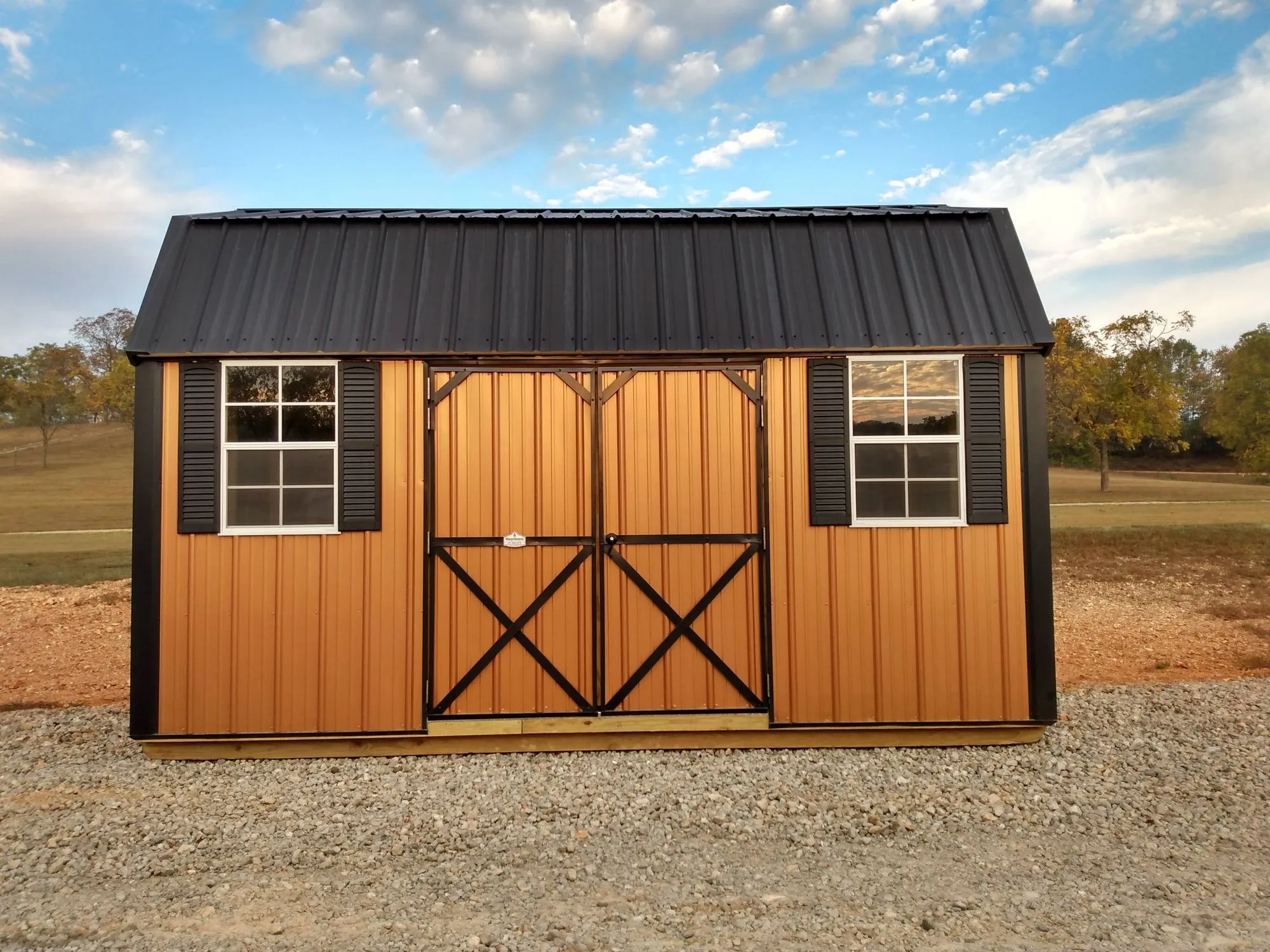 Lofted Garden Barn with woodgrain metal siding, black trim and roof, black X-braced doors, black shutters