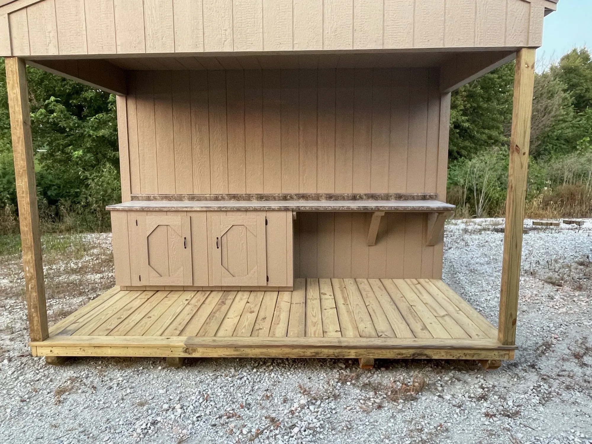 Close view of the covered porch: a wood deck, two posts and a potting bench with two cabinet doors